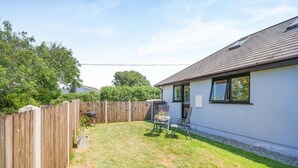 Un jardin avec une clôture en bois, un barbecue et une table avec des chaises.