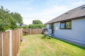 A backyard with a wooden fence, a barbecue grill, and a table with chairs. - 1 Bed in Nr Bude (oc-penke) (Crackington)