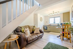 A modern living room with a leather sofa, a dining table with chairs, a staircase, and a kitchen area. - 1 Bed in Nr Bude (oc-penke) (Crackington)