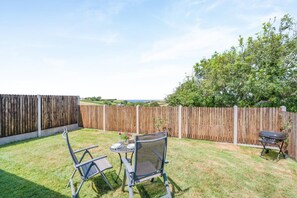 A backyard with a wooden fence, a table with chairs, and a barbecue grill. - 1 Bed in Nr Bude (oc-penke) (Crackington)