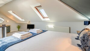 Une chambre avec un plafond en pente, des fenêtres de toit, un lit avec des serviettes, une commode, un téléviseur et un radiateur.