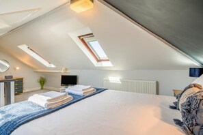 A bedroom with a sloped ceiling, skylights, a bed with towels, a dresser, a television, and a radiator. - 1 Bed in Nr Bude (oc-penke) (Crackington)