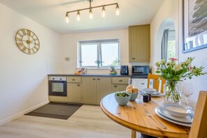 A modern kitchen with a built-in oven, a dining table set with plates, bowls, and a vase of flowers. - 1 Bed in Nr Bude (oc-penke) (Crackington)