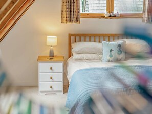 A bedroom with a bed, a nightstand, a lamp, and a window with curtains.
