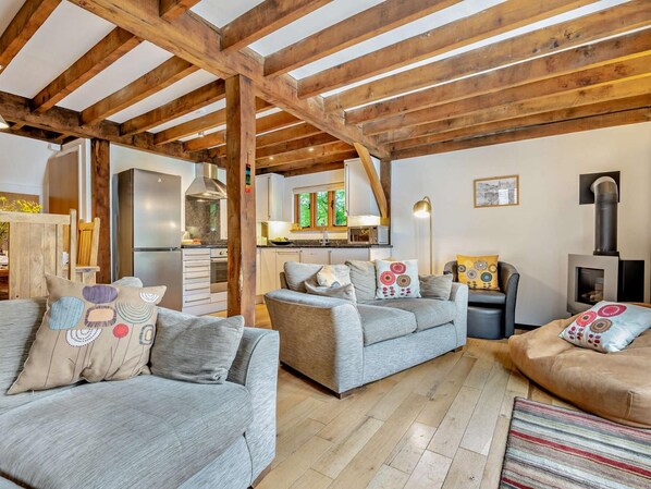 A cozy living room with wooden beams, a kitchen, and a fireplace.