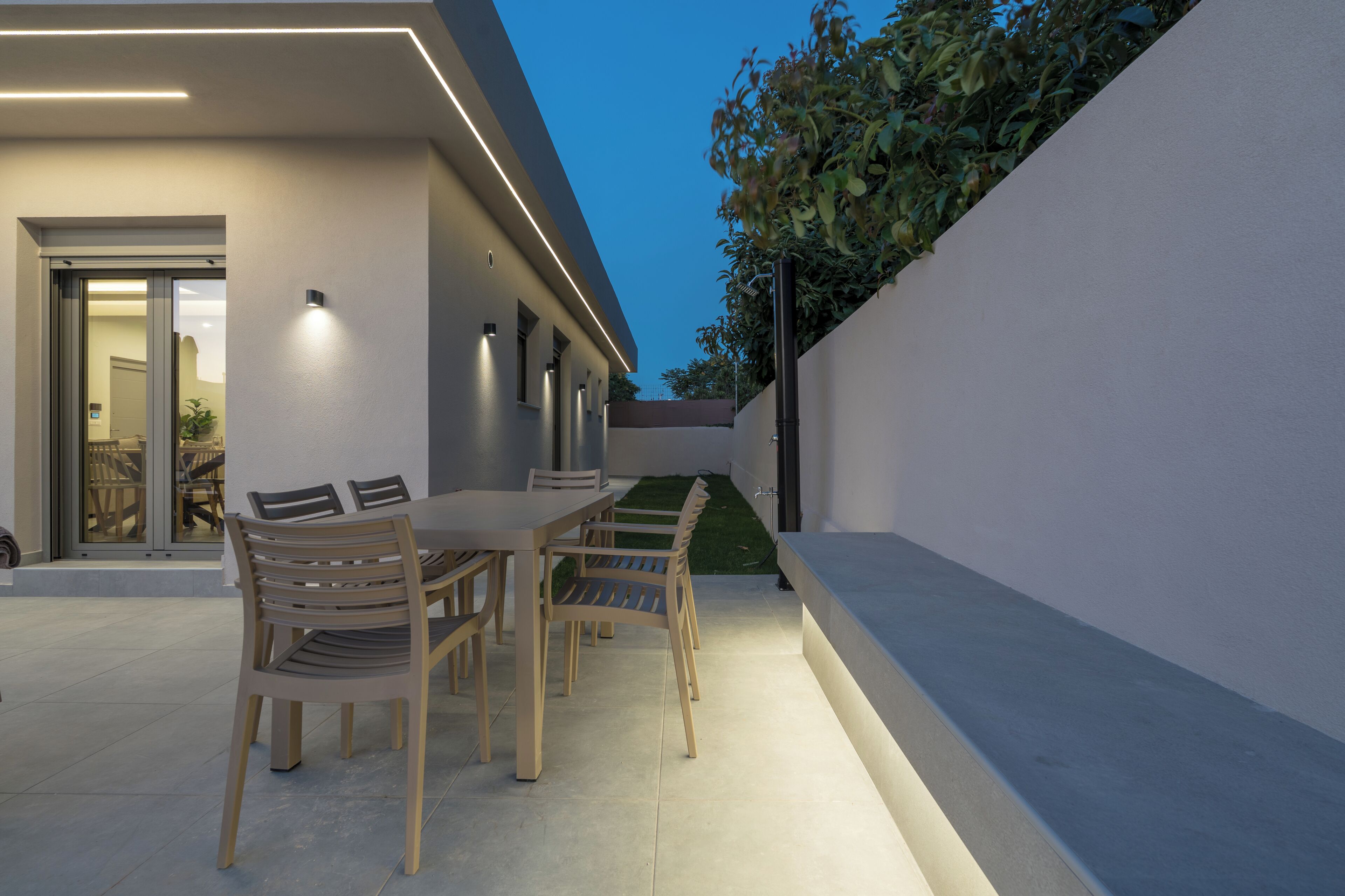 Un espacio de comedor al aire libre con una mesa, sillas, una puerta y un jardín pequeño junto a la pared.
