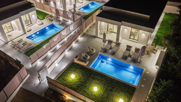 A modern house with two swimming pools, outdoor seating, and a well-lit patio area.