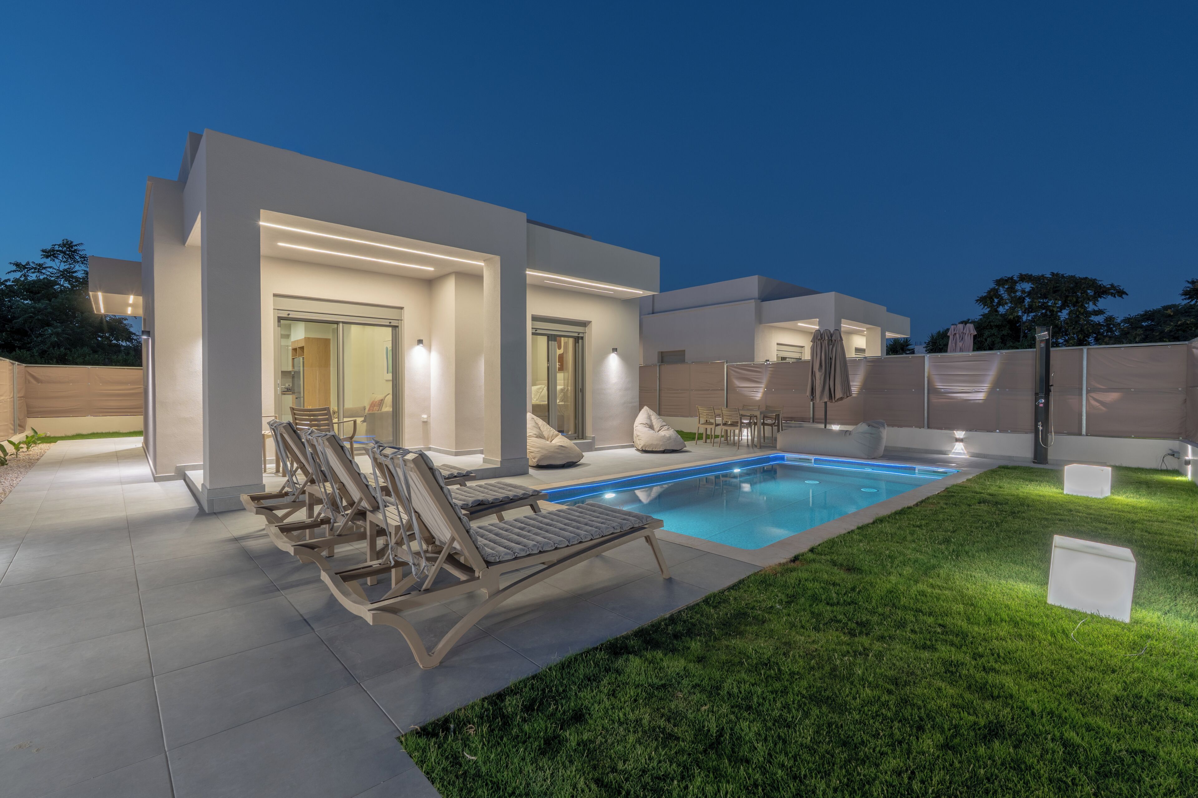 Ett modernt hus med en swimmingpool, utomhusmöbler och en väl upplyst uteplats.