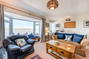 A living room with a view of the beach, a sofa, a coffee table, and a lamp. - 2 Bed in Bideford (oc-reefc) (Appledore)