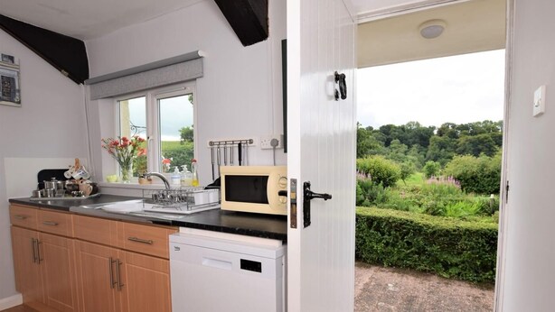 A kitchen with a dishwasher, a microwave, and a window with a view of a garden. - 2 Bed in Tiverton (oc-shayn) (Shillingford)