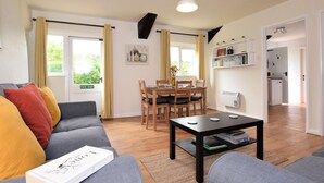 A modern living room with a grey sofa, a dining table, and a kitchen in the background. - 2 Bed in Tiverton (oc-shayn) (Shillingford)