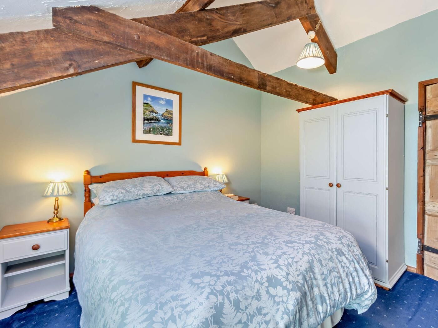 A bedroom with a bed, bedside lamps, a wardrobe, and a framed picture on the wall.
