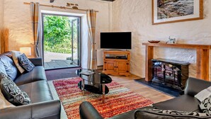 Ein Wohnzimmer mit Sofa, Couchtisch, Kamin, Fernseher und Blick ins Grüne durch die Glasdoor.