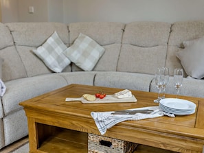 Ein Couchtisch aus Holz mit einem Käsebrett, Crackern und Tomaten, dazu Weingläser und Teller, auf einem Sofa mit karierten Kissen.