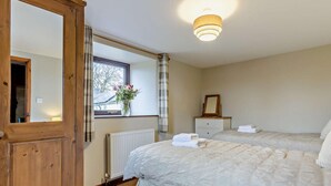 Een slaapkamer met twee bedden, een houten garderobe, een nachtkastje met spiegel en een raam met gordijnen.