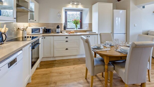 Een moderne keuken met witte kastjes, een houten eettafel en een inbouwoven.