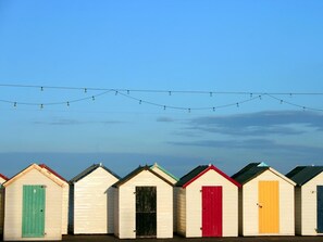 Eine Reihe von Strandkörben mit unterschiedlich farbigen Türen, ein klarer Himmel und Lichterketten darüber.