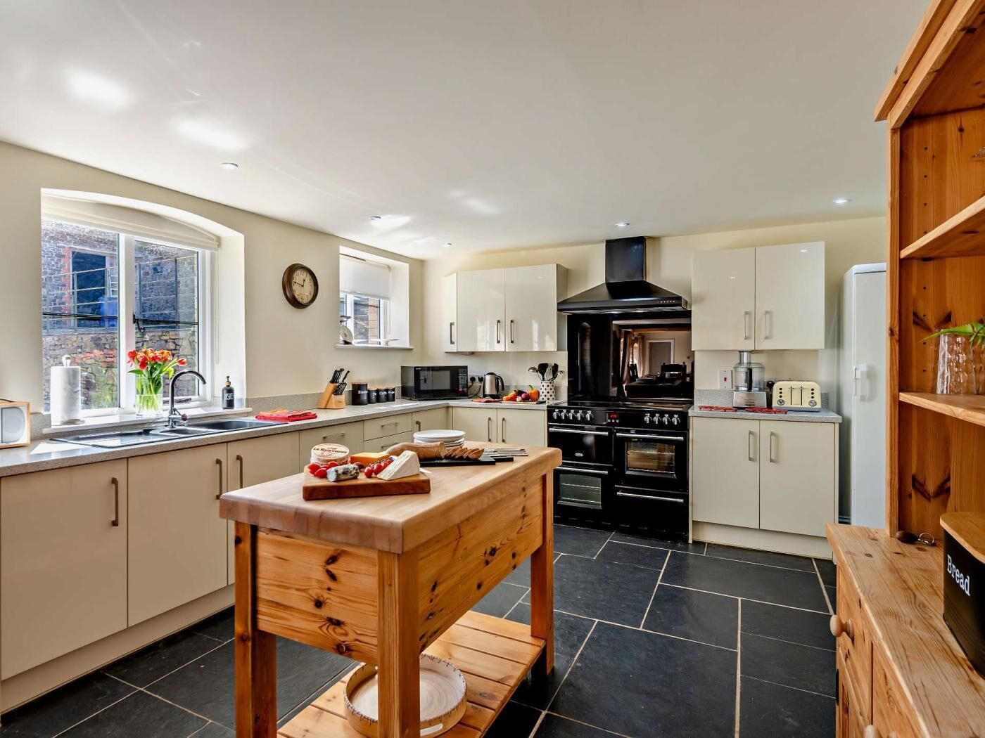 A modern kitchen with a central island, black stove, white cabinets, and a window with a view.