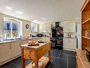 A modern kitchen with a central island, black stove, white cabinets, and a window with a view. - 6 Bed in Bideford (oc-thorn) (Buckland Brewer)