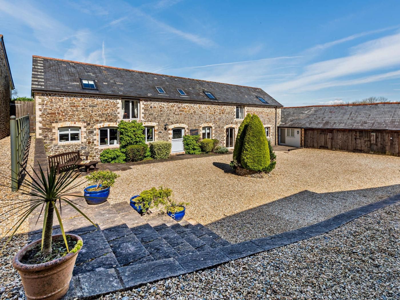 A stone building with multiple windows, a gravel courtyard, and potted plants.