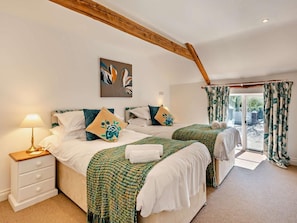 A bedroom with two beds, a nightstand, a lamp, a painting, and a view through a door. - 6 Bed in Bideford (oc-thorn) (Buckland Brewer)
