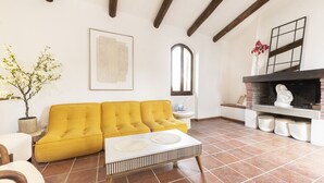 A living room with a yellow sofa, a white coffee table, a fireplace, and a potted plant.