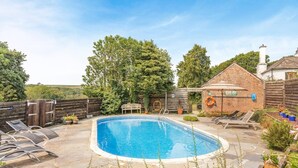 Una piscina con lettini, una recinzione in legno e un edificio in mattoni con un ombrellone.