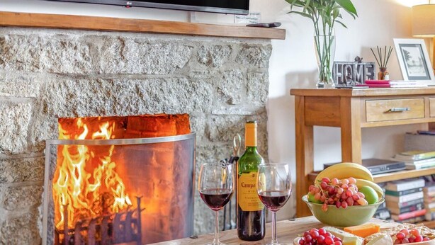 Un caminetto acceso, una bottiglia di vino, bicchieri e un vassoio di frutta su un tavolo di legno.