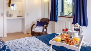 Una camera d'albergo con un letto, una sedia, un vassoio con articoli per la colazione e una finestra con tende.