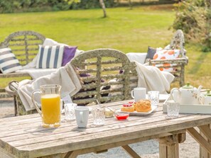 A wooden table with a glass of orange juice, a plate of scones, and a teapot set on a garden patio. - 3 Bed in Lifton (oc-tcoah) (Broadwoodwidger)