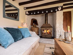 A cozy room with a sofa, a fireplace, a mirror, and a wooden table with glasses and a bottle. - 2 Bed in Bideford (oc-tcvalen) (Weare Giffard)