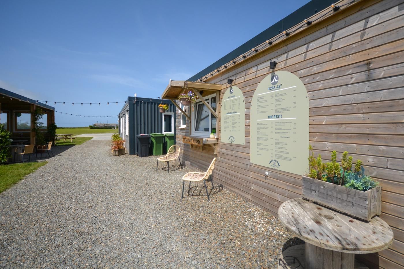 A rustic building with a gravel patio, wooden benches, and a wooden table.