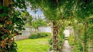 Een tuinpad met een houten pergola, een stenen muur en een gazon.