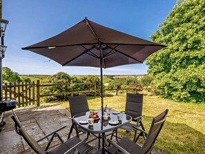 Een terras met een tafel, vier stoelen, een grote parasol en een barbecue.