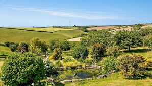 Een landelijk landschap met glooiende groene velden, een klein vijvertje en een houten omheining.