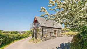 A stone house with a balcony, a paved driveway, and surrounding greenery. - 1 Bed in Looe (oc-couvw) (Lansallos)