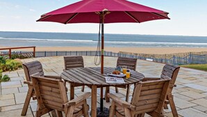 Ein Holztisch mit Stühlen und einem roten Sonnenschirm mit Blick auf einen Strand.