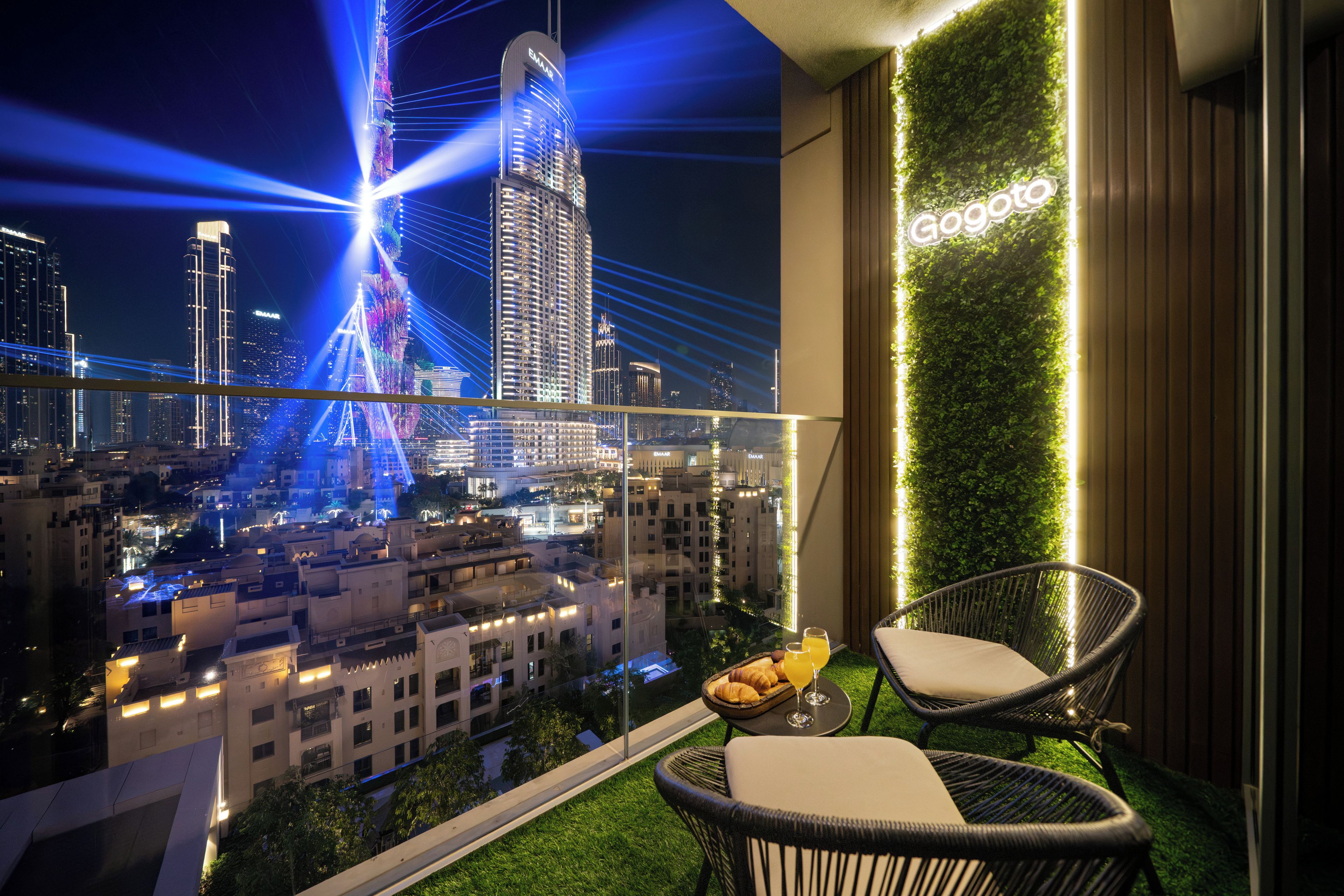 Un balcon offrant une vue sur une ville illuminée la nuit, avec notamment un bâtiment imposant dont les contours sont mis en valeur par des jeux de lumière.