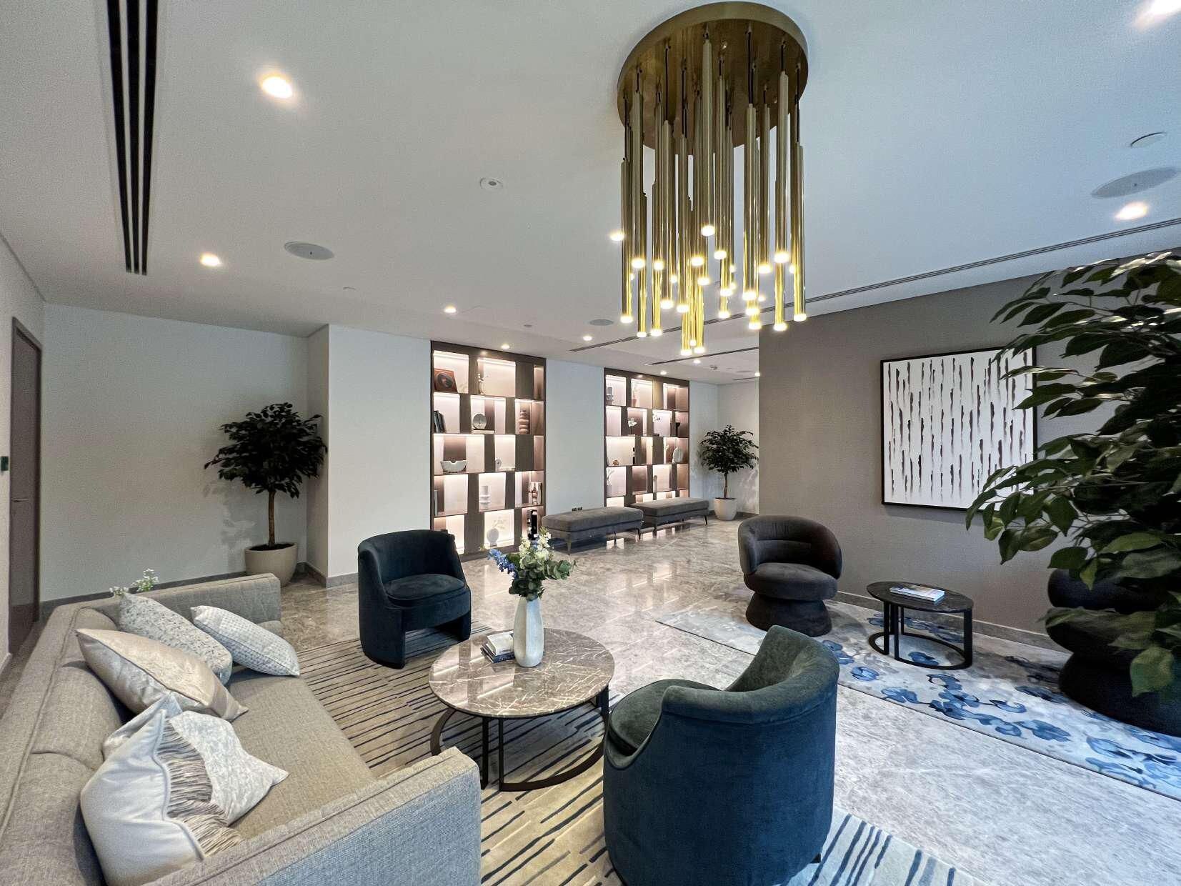 A modern lobby with a sofa, chairs, a coffee table, a bookshelf, and a large plant.