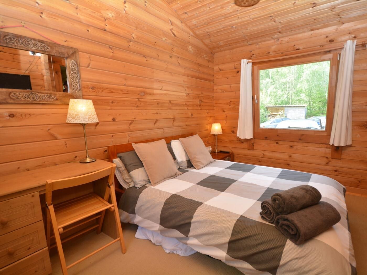Une chambre de style cabane en bois, avec un lit, des lampes de chevet, un petit bureau et une fenêtre avec des rideaux.