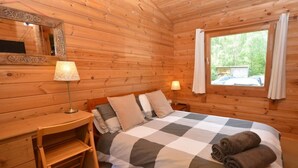 En stuga med träpanel, ett rum med en säng, sänglampor, ett litet skrivbord och ett fönster med gardiner.