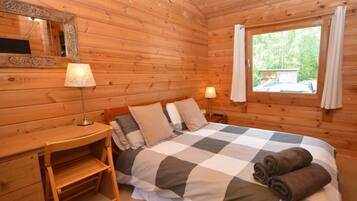 Une chambre de style cabane en bois, avec un lit, des lampes de chevet, un petit bureau et une fenêtre avec des rideaux.