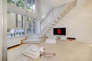 Quarto de hotel moderno com uma janela grande, uma escada, uma TV de tela plana e um logotipo no chão.