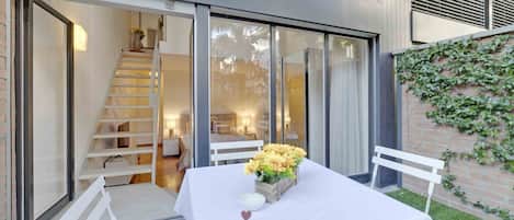 A dining area with a table set for two, a staircase, and a view of the interior through glass doors.