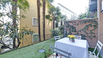 Un patio con una mesa y sillas, rodeado de plantas y un muro de ladrillo.