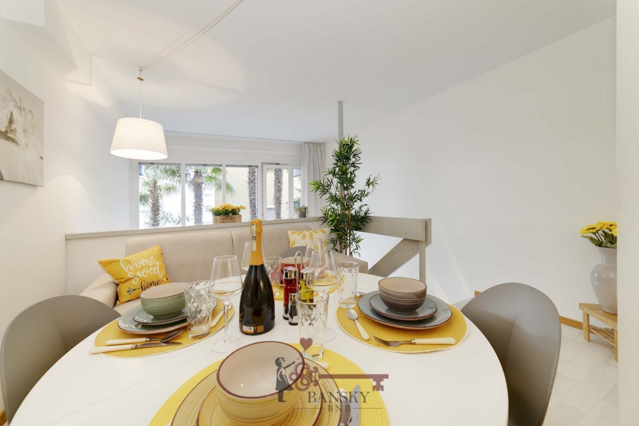 Un coin repas avec une table mise pour le dîner, une bouteille de vin et un vase rempli de fleurs.