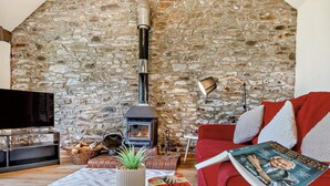 Un salon chaleureux avec un mur en pierre, une cheminée, un canapé rouge, un téléviseur et une table garnie de pâtisseries.