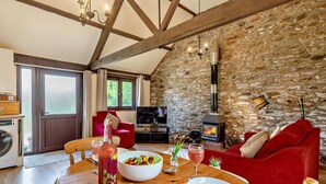 Un salon chaleureux avec un mur en pierre, une cheminée, une table à manger dressée pour deux personnes et un canapé rouge.