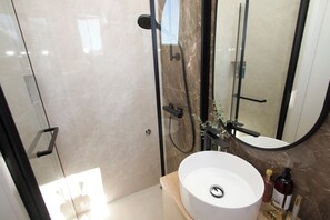 Ein modernes Badezimmer mit einer gläsernen Duschkabine, einem weißen Waschbecken und einem Spiegel.