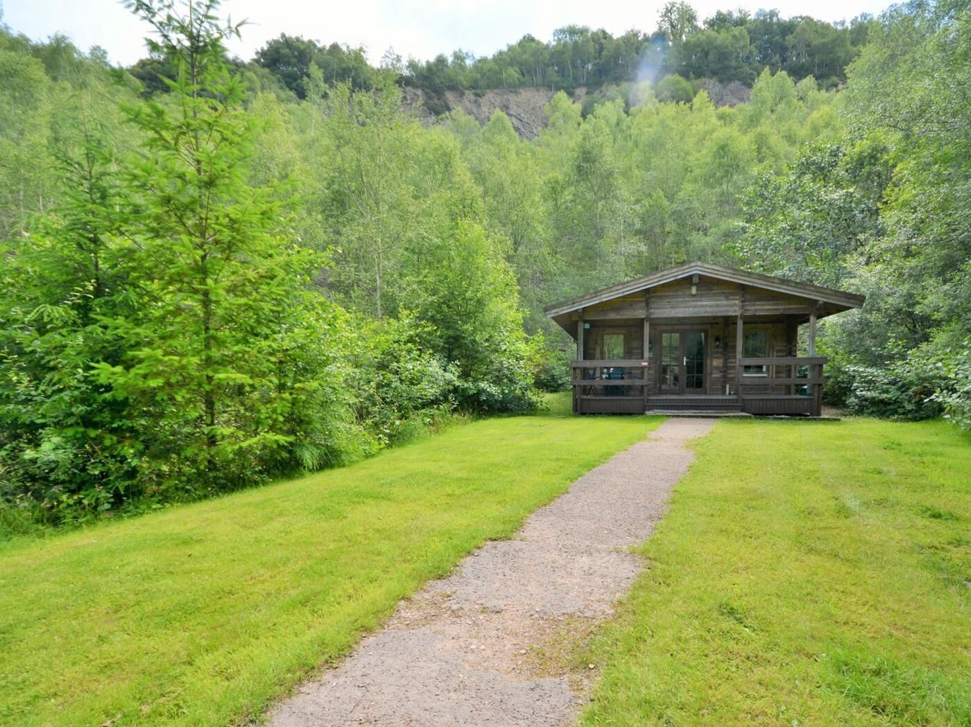 Un chalet rustique doté d’un porche, entouré d’une végétation luxuriante et accessible par un chemin de gravier.
